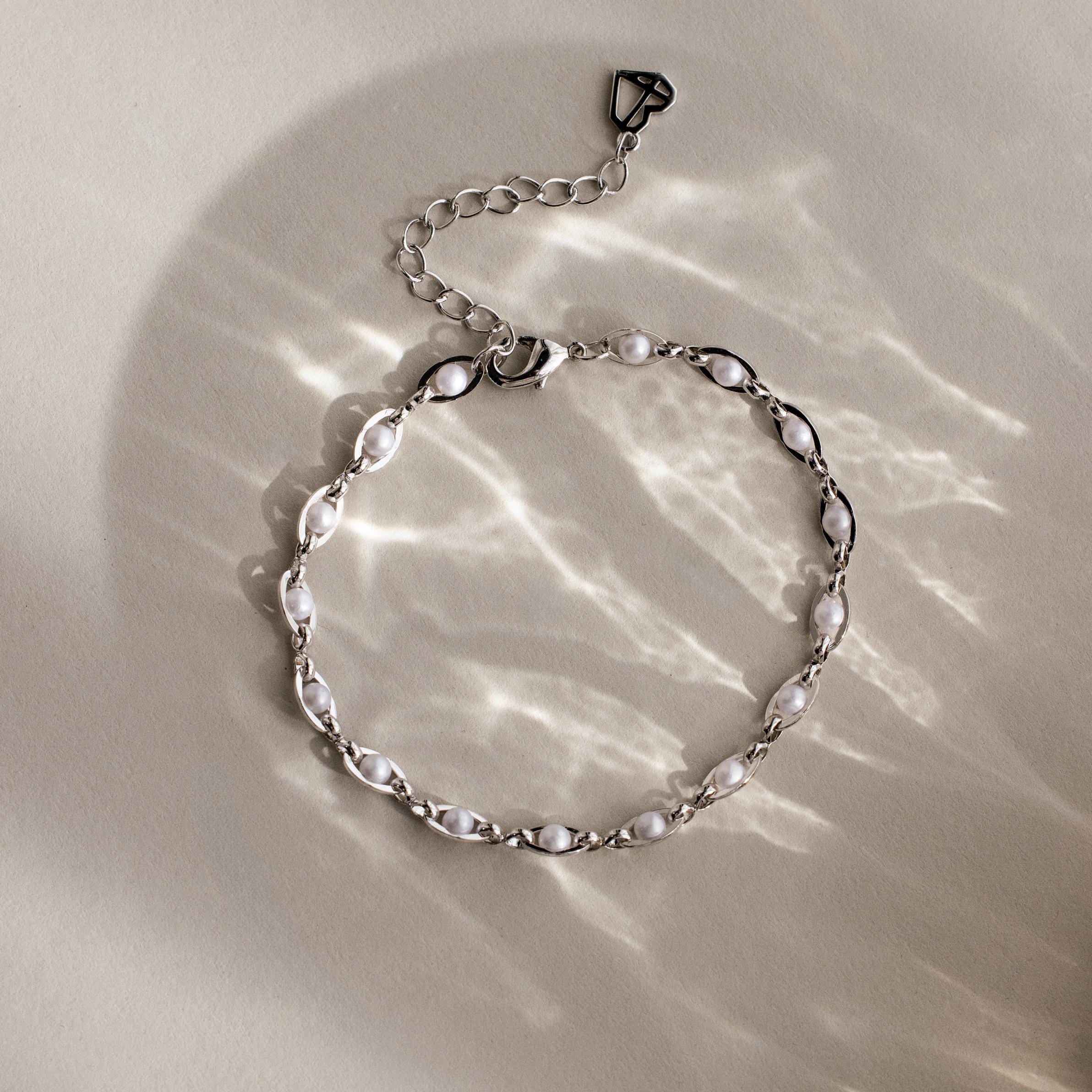 The Eternity Pearl Bracelet in Sterling Silver features a silver infinity chain with white pearls. Displayed on a neutral surface, its graceful charm is enhanced by soft light reflections, merging elegance with timeless style.