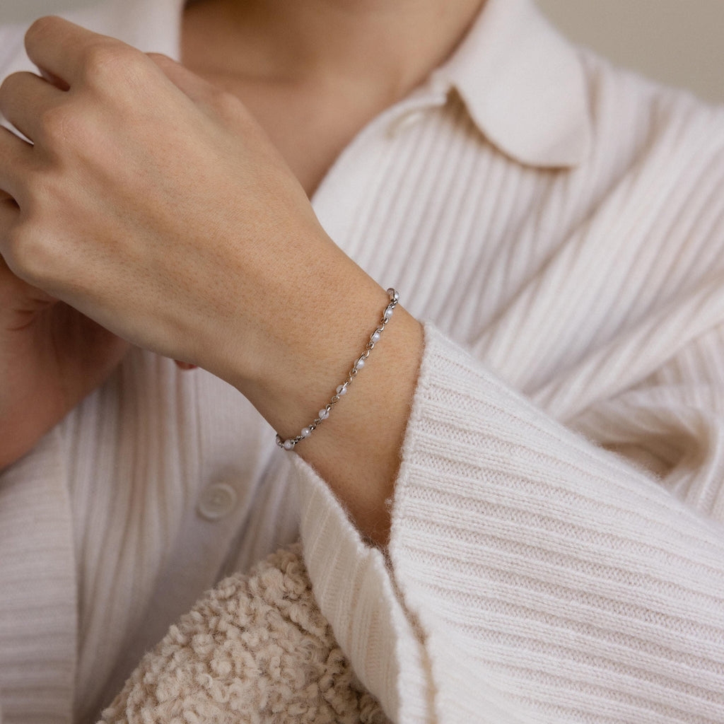 A person wearing the Eternity Pearl Bracelet in Sterling Silver and a cream ribbed shirt holds a textured beige fabric.