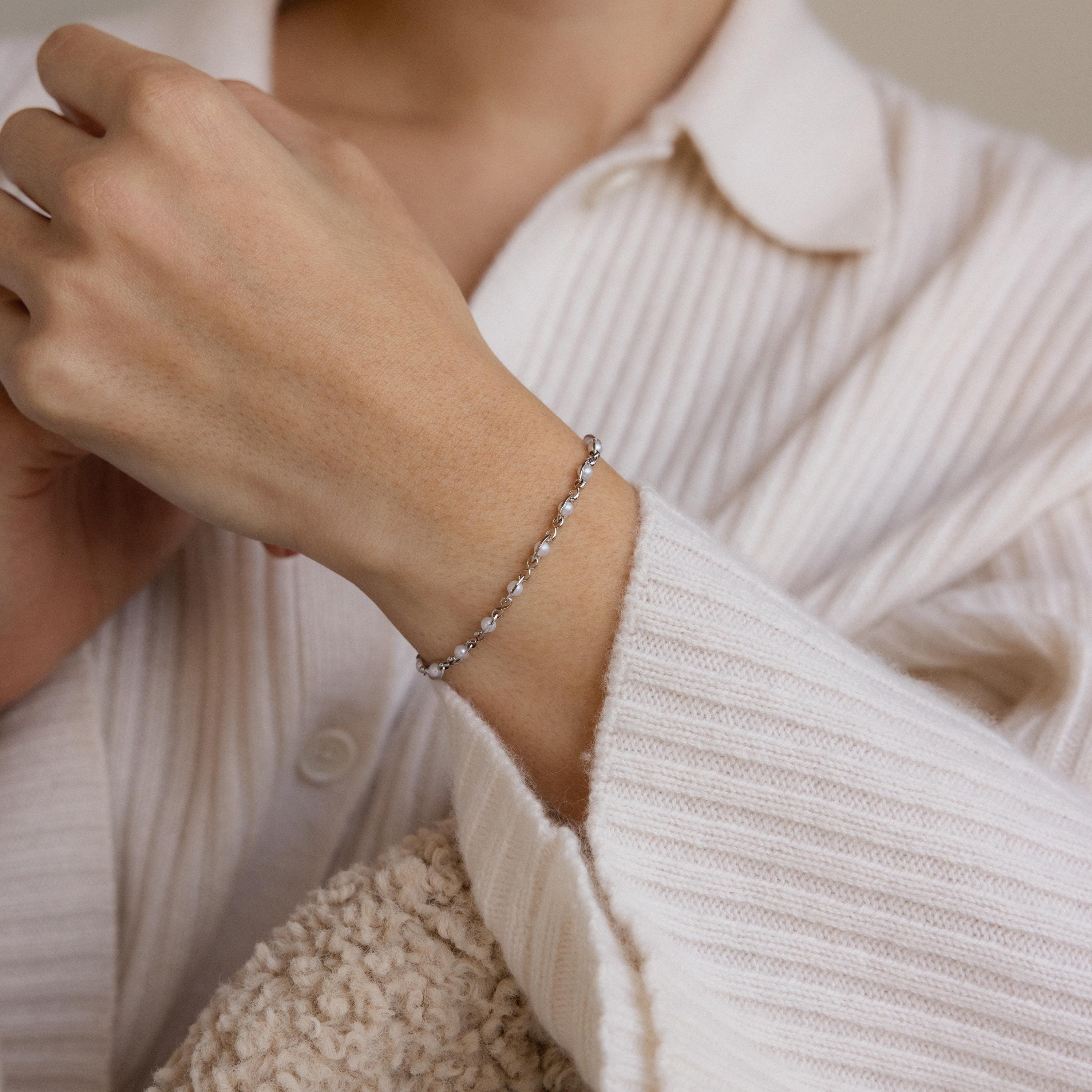 A person wearing the Eternity Pearl Bracelet in Sterling Silver and a cream ribbed shirt holds a textured beige fabric.