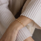 A person wearing the Eternity Pearl Bracelet in 18K Gold, featuring an elegant infinity chain detail, paired with a cream ribbed sweater.