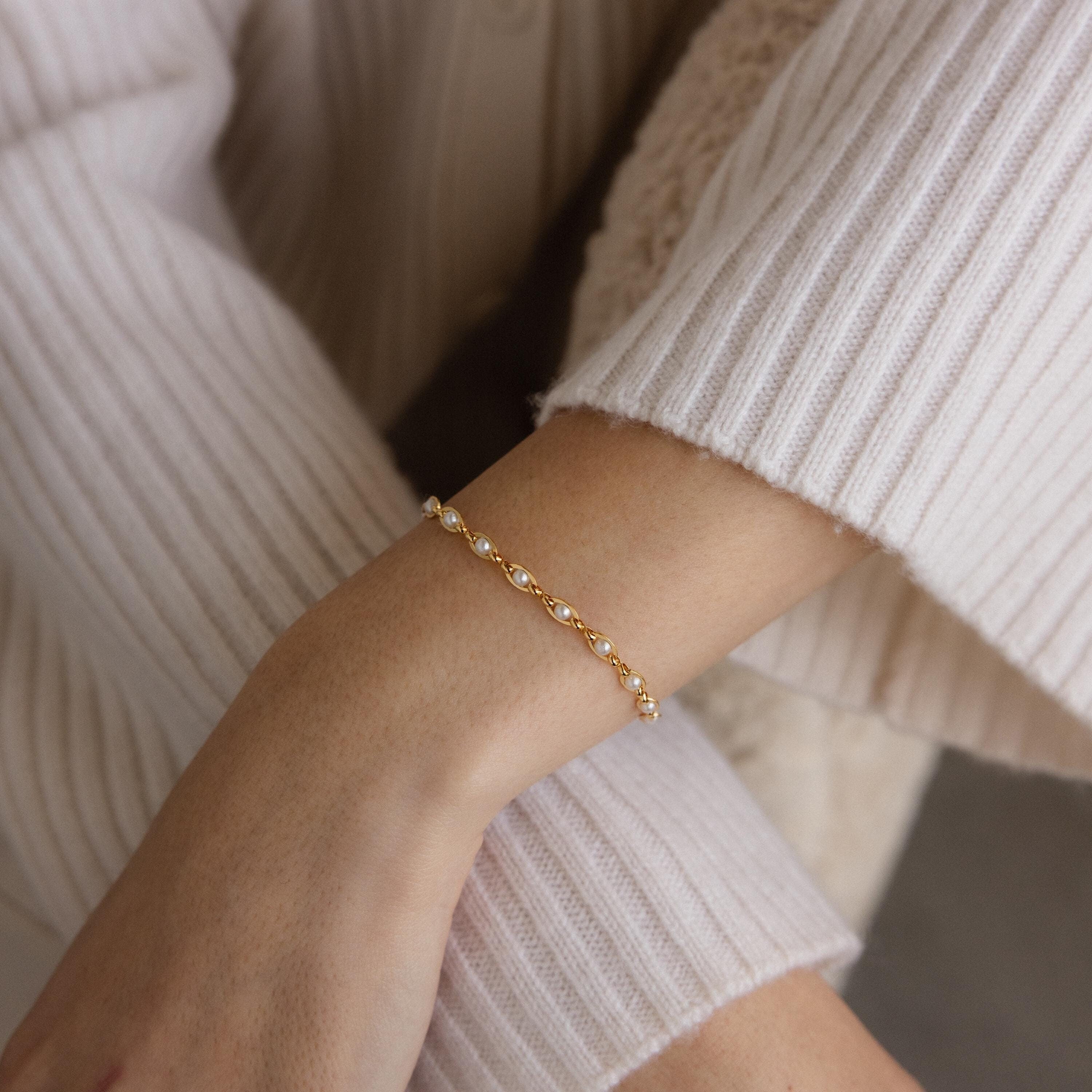A person wearing the Eternity Pearl Bracelet in 18K Gold, featuring an elegant infinity chain detail, paired with a cream ribbed sweater.