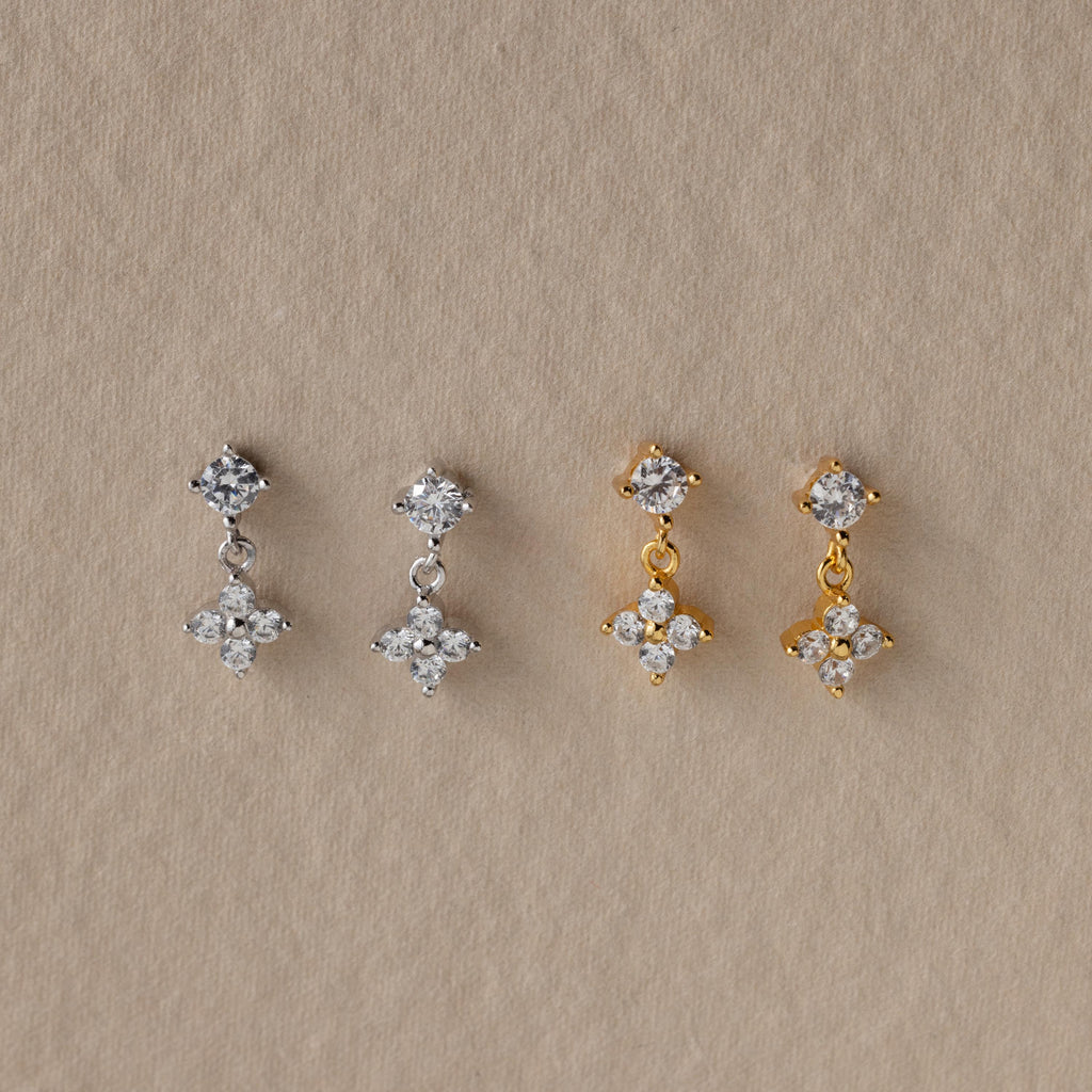 Two pairs of dangling earrings—one silver, one gold—with crystal floral designs make a stunning Mother's Day gift. Shown on a beige background, they pair beautifully with Ivy Flower Flat Back Studs.