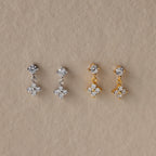 Two pairs of dangling earrings—one silver, one gold—with crystal floral designs make a stunning Mother's Day gift. Shown on a beige background, they pair beautifully with Ivy Flower Flat Back Studs.