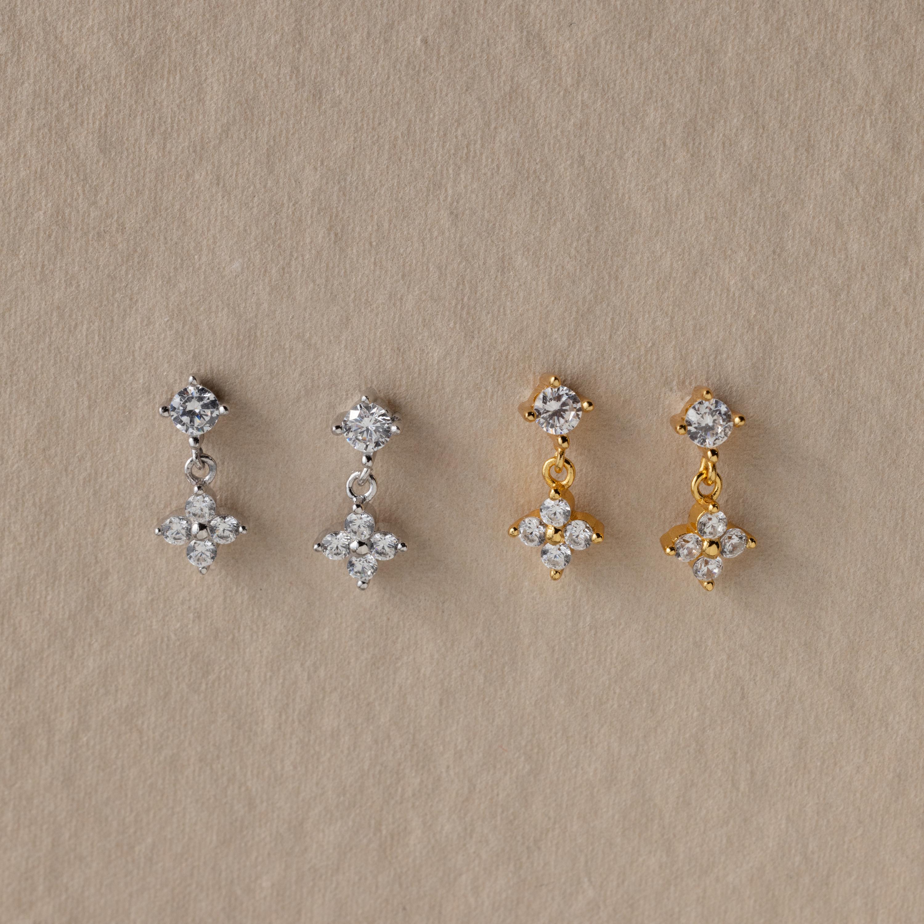Two pairs of dangling earrings—one silver, one gold—with crystal floral designs make a stunning Mother's Day gift. Shown on a beige background, they pair beautifully with Ivy Flower Flat Back Studs.
