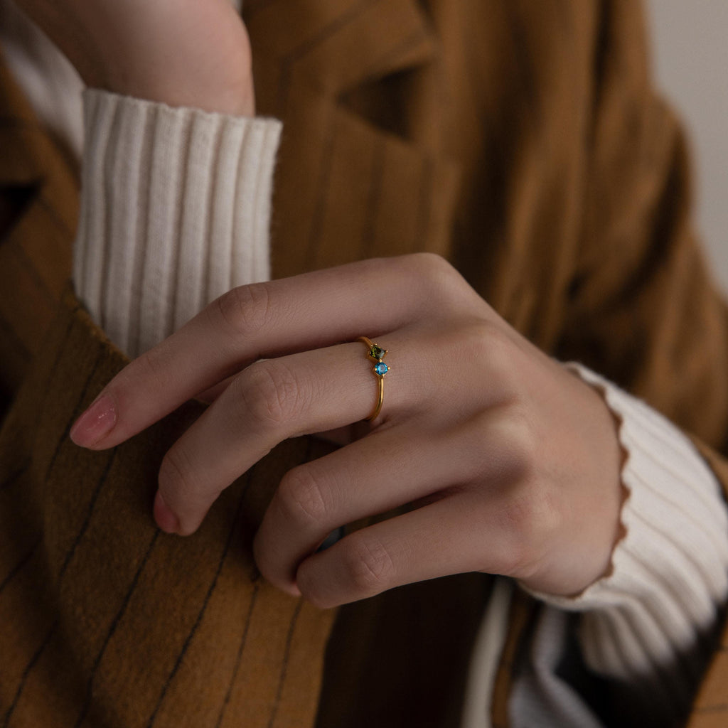 A hand wearing the Toi et Moi Princess Birthstone Ring with a blue stone, paired with a brown pinstripe blazer and white sweater.