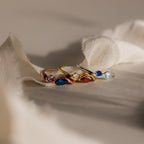 The Toi et Moi Infinity Birthstone Ring shines in gold and silver atop soft beige fabric, its customizable gemstones sparkling in gentle light—a perfect symbol of love and personal connection.