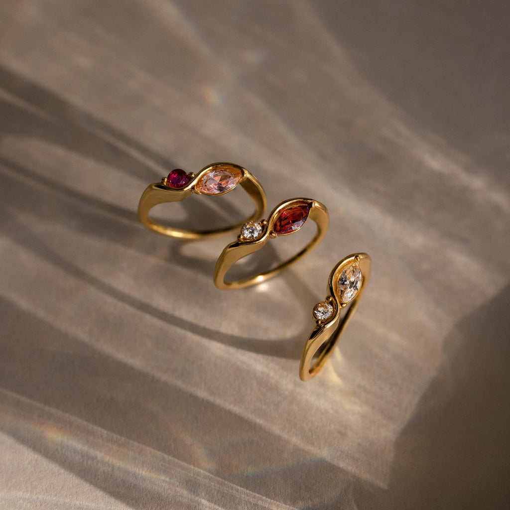 The Toi et Moi Infinity Birthstone Rings, each adorned with marquise-shaped personalized gemstones, are elegantly displayed on a softly lit neutral surface—a stunning symbol of love.