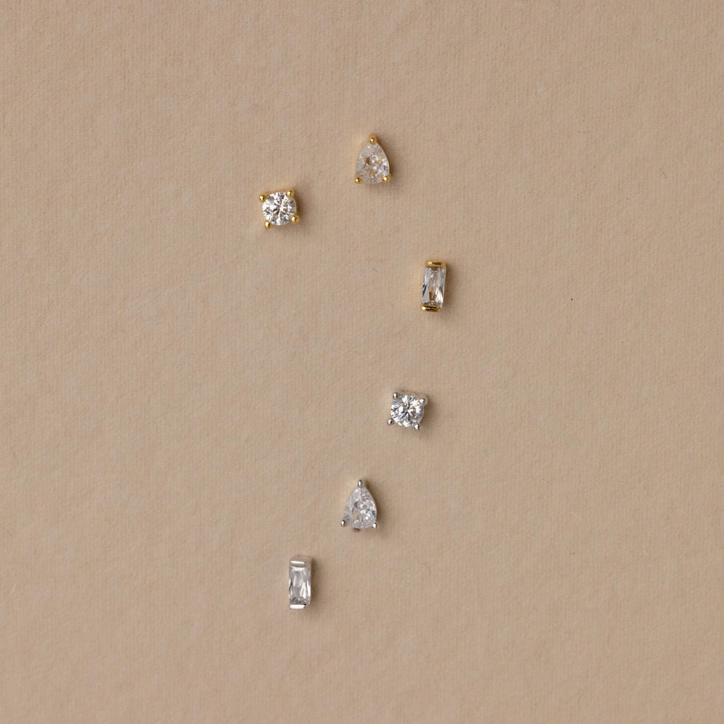The Mixed Diamond Flat Back Stud Set features six small gold and silver flat back stud earrings with clear stones, arranged on a beige background.