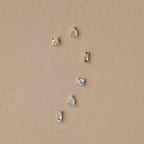 The Mixed Diamond Flat Back Stud Set features six small gold and silver flat back stud earrings with clear stones, arranged on a beige background.