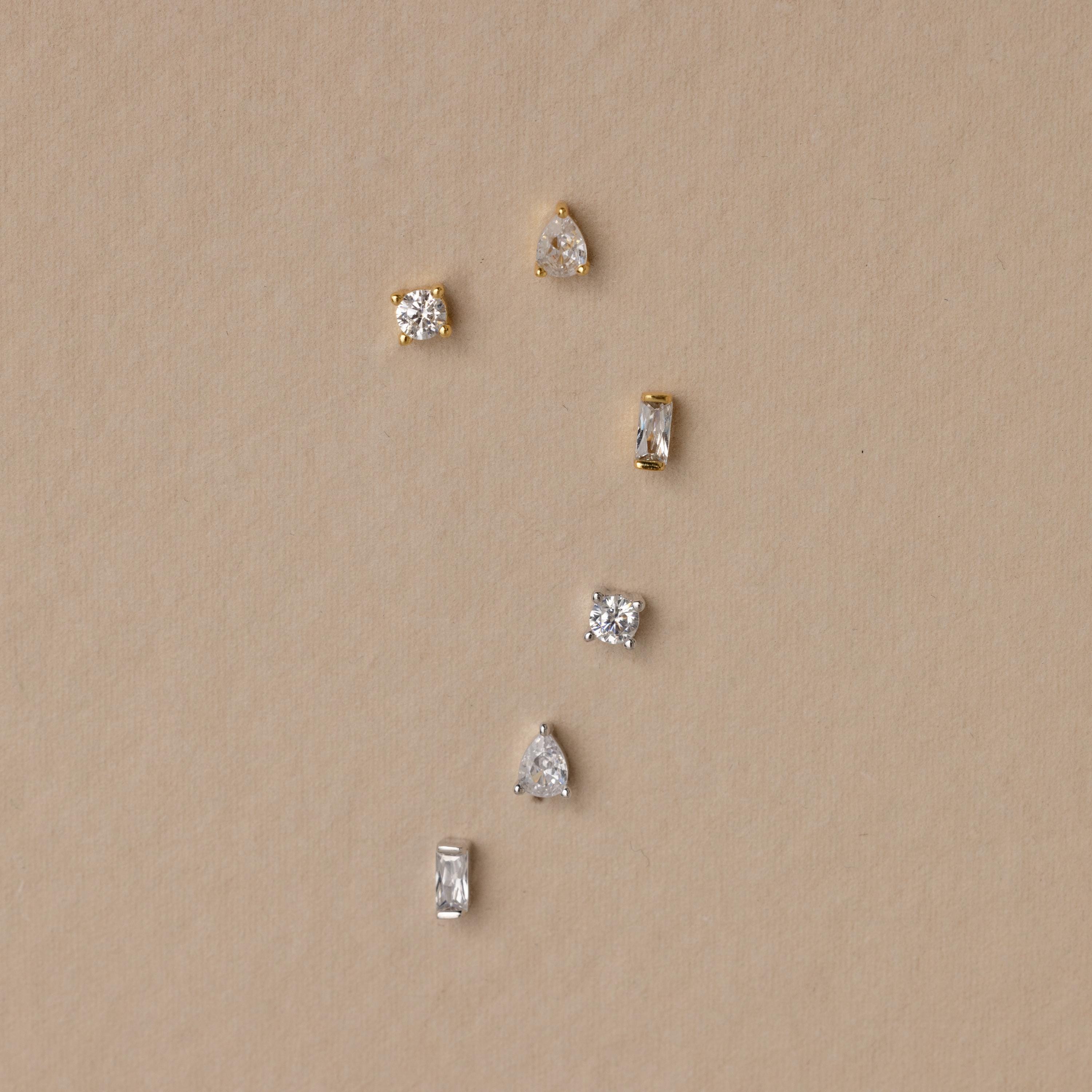 The Mixed Diamond Flat Back Stud Set features six small gold and silver flat back stud earrings with clear stones, arranged on a beige background.