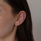 Close-up of a person's ear wearing the Mixed Diamond Flat Back Stud Set—four small, uniquely shaped diamond studs—with wet, dark hair.