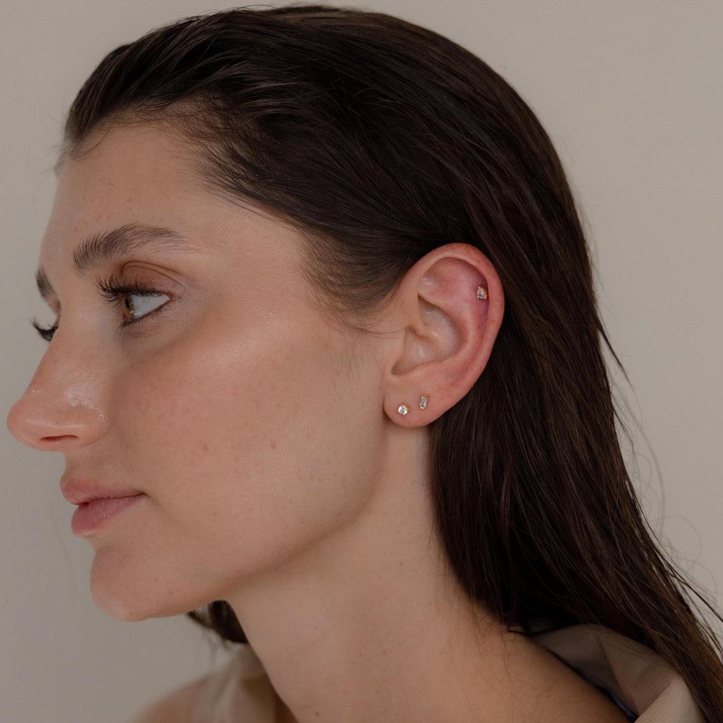A woman with wet hair wears the Mixed Diamond Flat Back Stud Set and small gold hoops on her earlobe and cartilage, set against a neutral background.
