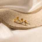 Gold earrings with white stones, like our Marquise Opal Flat Back Studs, displayed on a speckled stone surface with soft beige fabric in the background—a perfect gift for her.