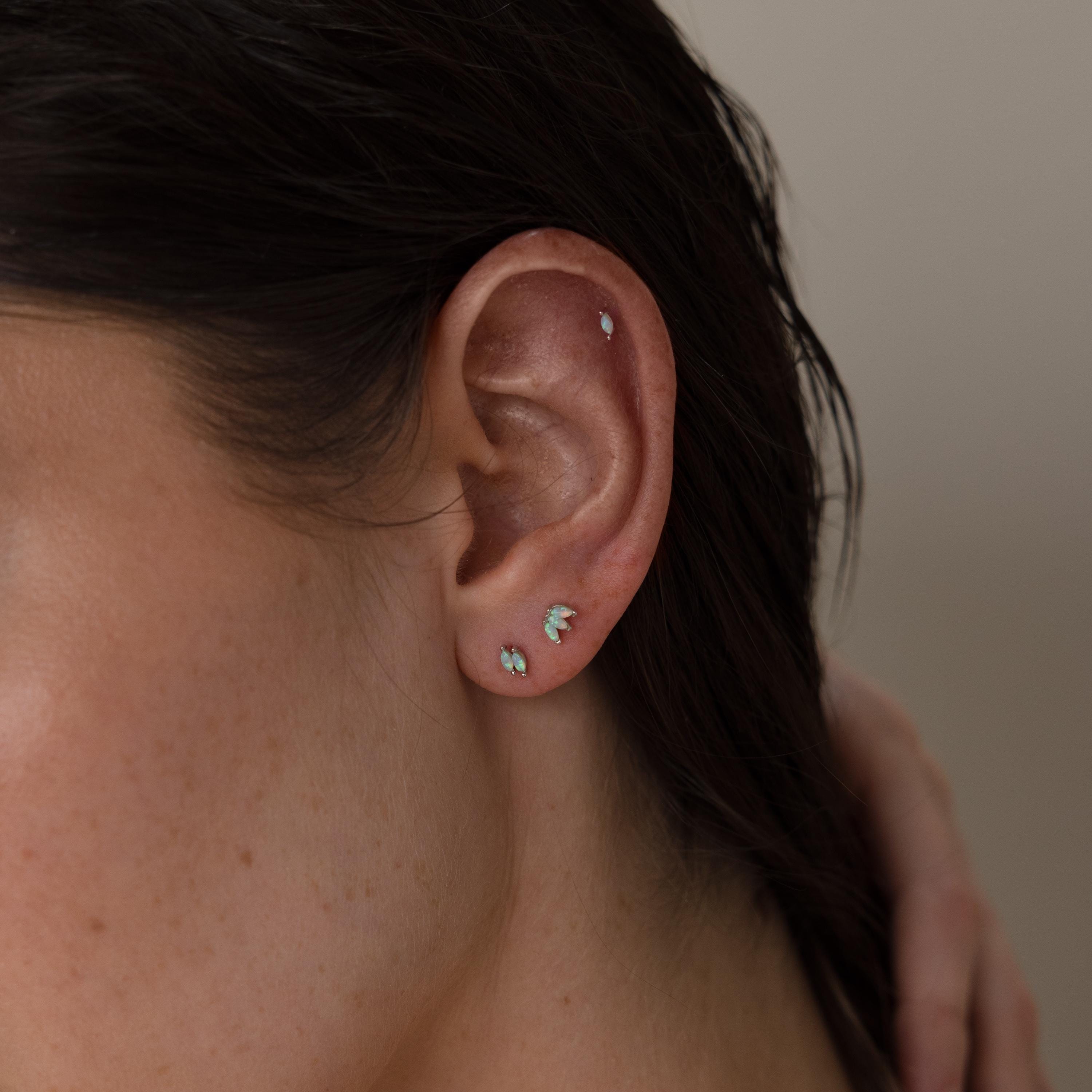 Close-up of a person's ear with three gemstone earrings and Marquise Opal Flat Back Studs adorning the upper ear—a stylish earring set, perfect as a Gift for Her.