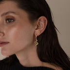 A woman with brown hair wears a gold snake-shaped earring and two smaller gold earrings, including the Pave Snake Charm Hoops, in her ear.