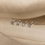 The Pave Assortment Flat Back Set features four earrings, each with a distinct crystal shape, displayed on cream fabric. This elegant set brings sparkle and style to any look.