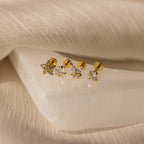 The Pave Assortment Flat Back Set features three pairs of gold stud earrings with sparkling stones, including pave diamond flat-back studs, displayed on a white textured surface.