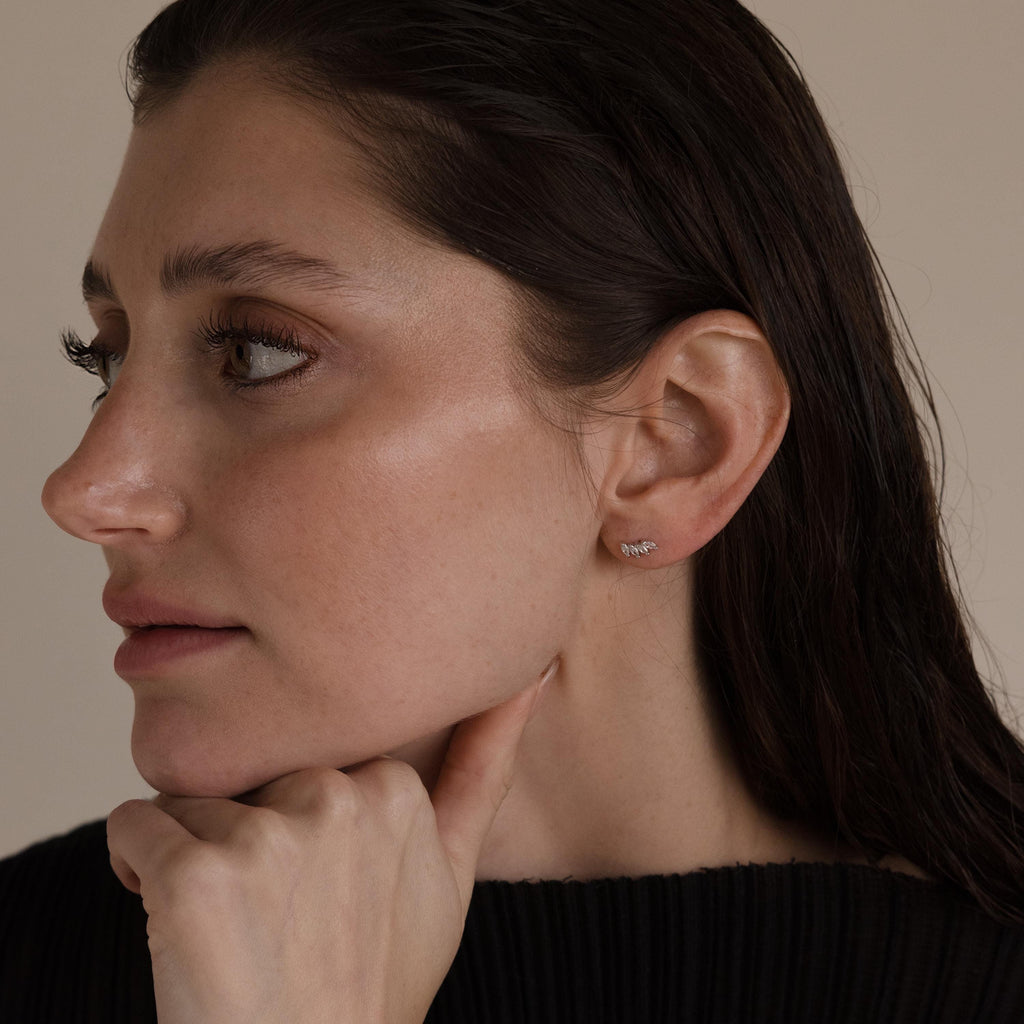 Woman with wet dark hair, in a black top and sparkling Marquise Diamond Climbers, rests her chin on her hand.