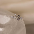 The Marquise Diamond Climbers are silver earrings with small, leaf-shaped crystals, evoking elegance and making a stunning wedding jewelry choice, beautifully presented on smooth, translucent stone.