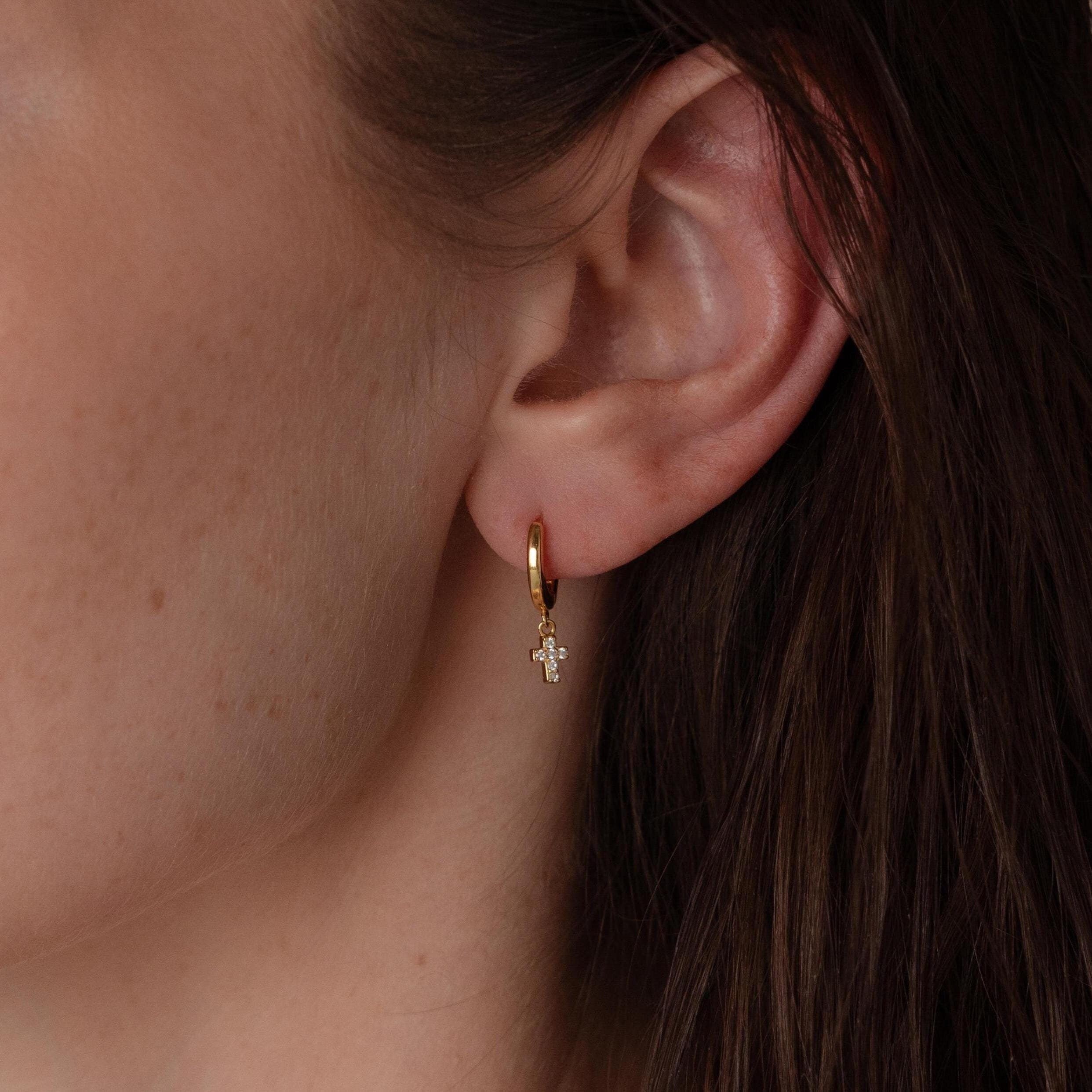 Close-up of a woman's ear adorned with Pave Cross Huggies—dainty hoops featuring a dangling cross charm.