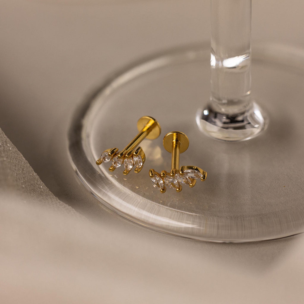 A pair of Marquise Diamond Climbers, perfect as wedding jewelry, rests on a clear glass coaster.