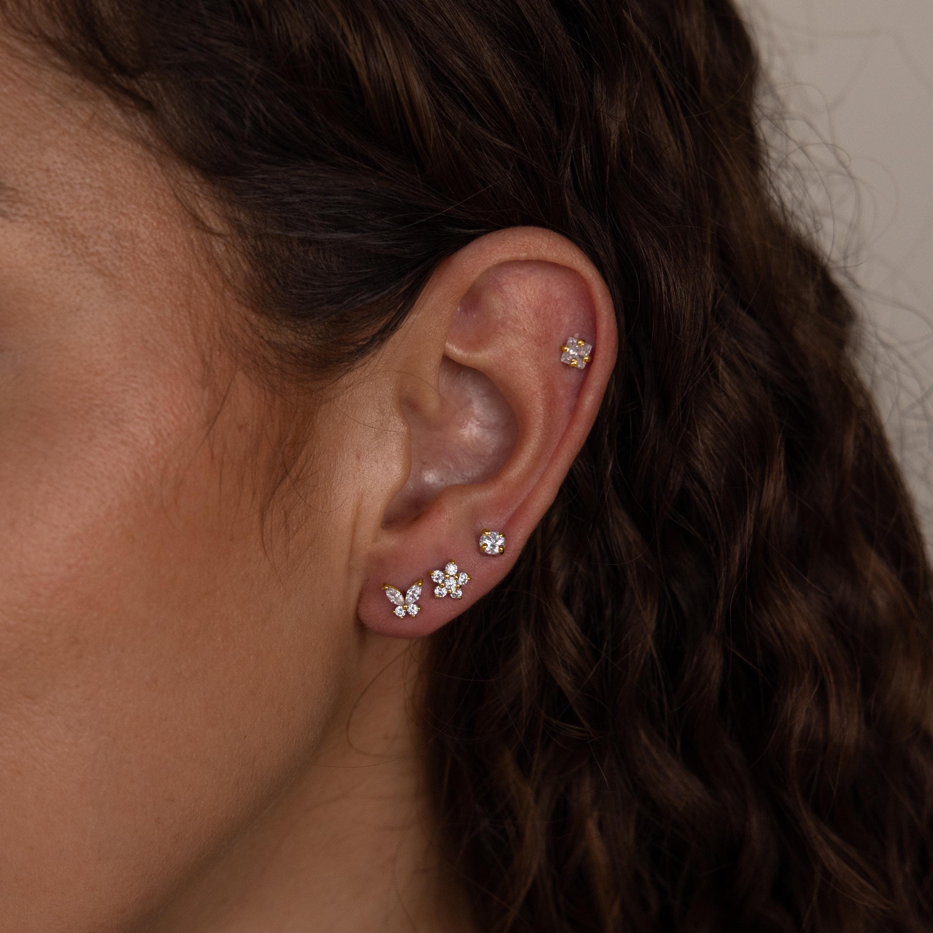 Close-up of a woman's ear wearing the Pave Assortment Flat Back Set, featuring pave diamond studs and flower-shaped earrings on her lobe and cartilage.