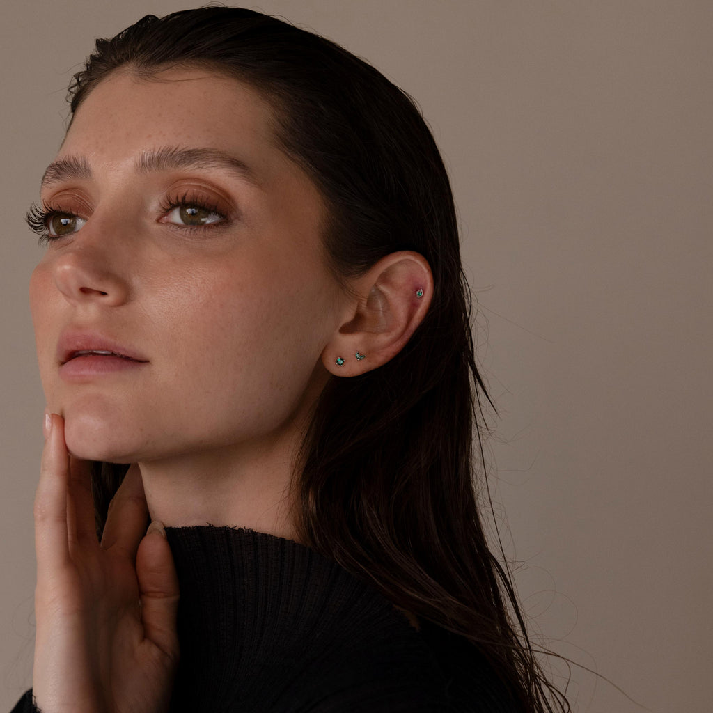 A woman with wet, dark hair in a black top touches her neck, showcasing the elegant Emerald Flat Back Earring Set.