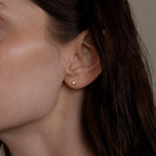 Close-up of a woman's ear wearing Small Diamond Bezel Flatback Studs, with part of her cheek and dark hair visible.
