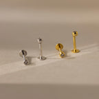 Two pairs of Small Diamond Bezel Flatback Studs—one in silver and one in gold, each with clear stones—are displayed on a beige surface.