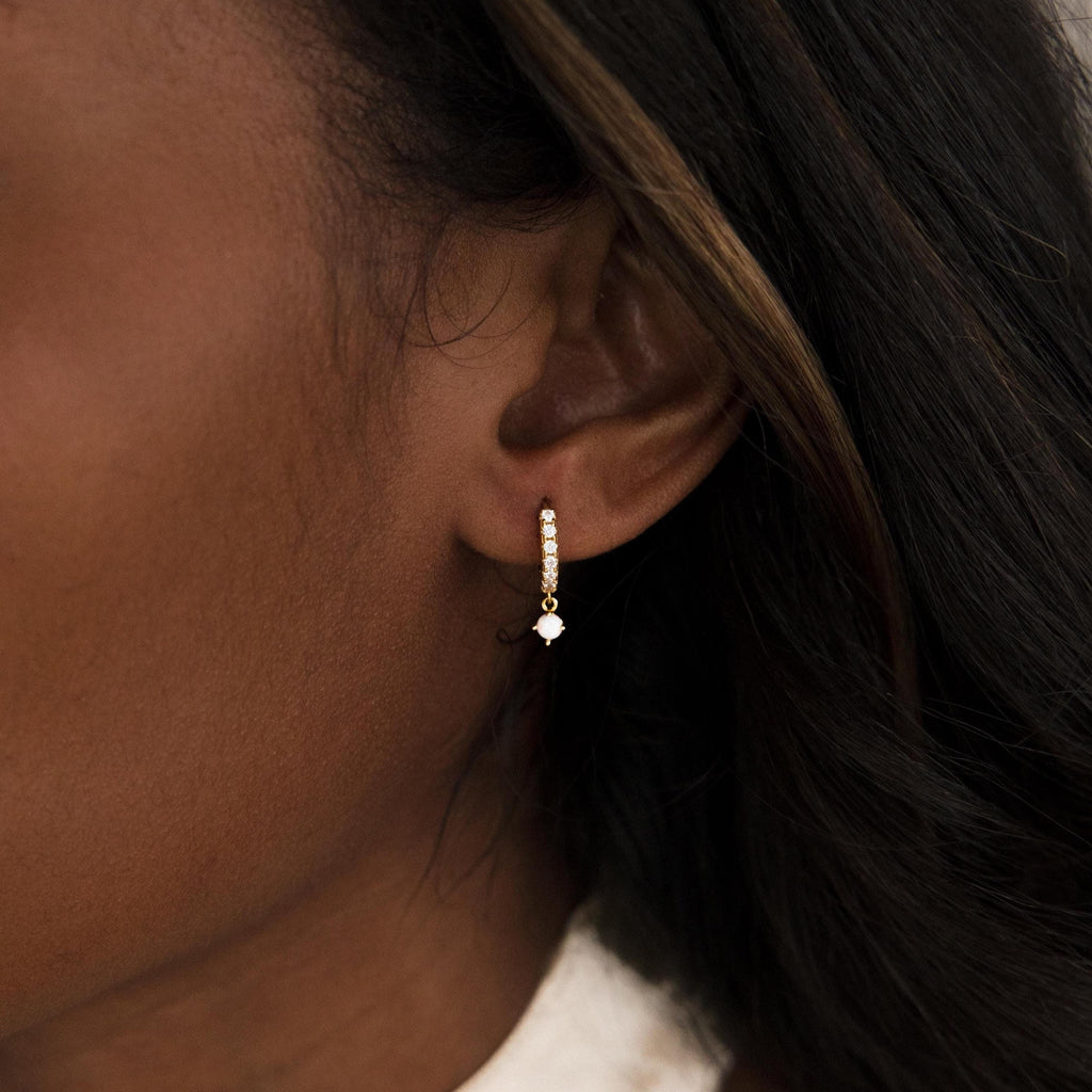 Close-up of a woman's ear wearing the Pave Opal Drop Huggies—sleek gold hoops featuring sparkling white stones.