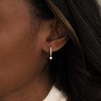 Close-up of a woman's ear wearing the Pave Opal Drop Huggies—sleek gold hoops featuring sparkling white stones.