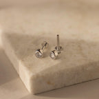 Showcased on a light stone surface, the Medium Diamond Bezel Flatback Studs feature silver settings with round clear gemstones—an elegant addition to any jewelry collection.