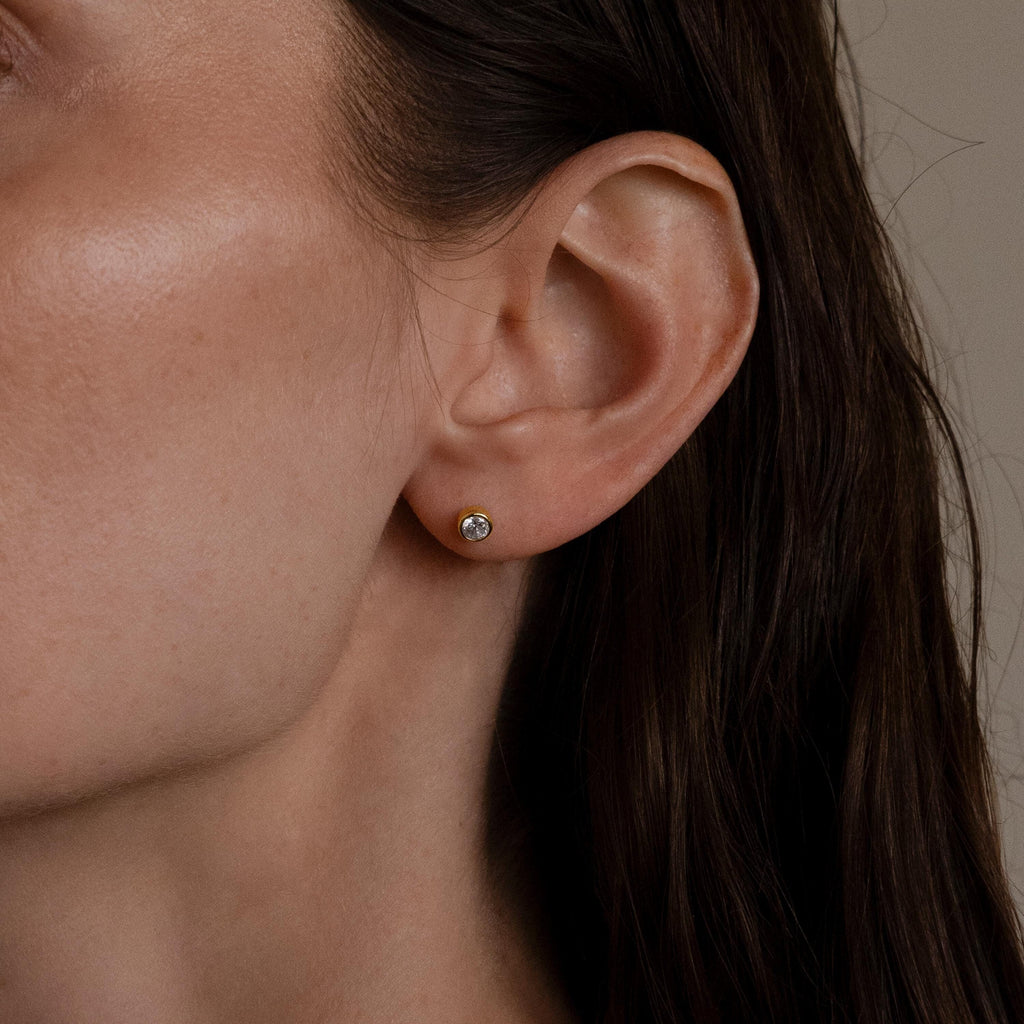 A woman's ear adorned with Medium Diamond Bezel Flatback Studs, adding a sparkling touch to any jewelry collection.