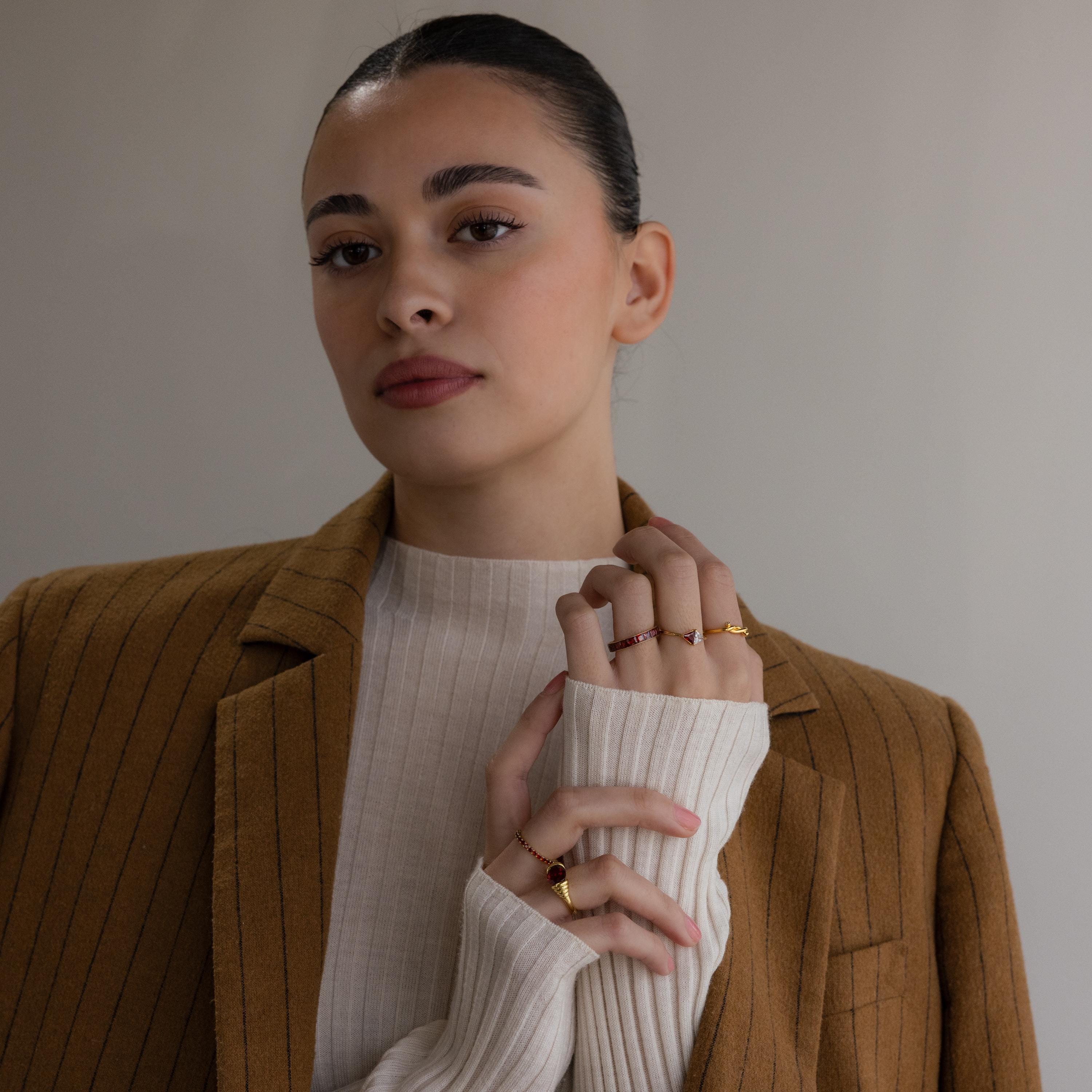 A woman in a brown pinstripe blazer and cream sweater showcases the Toi et Moi Triangle Birthstone Ring on her hand against a neutral background.