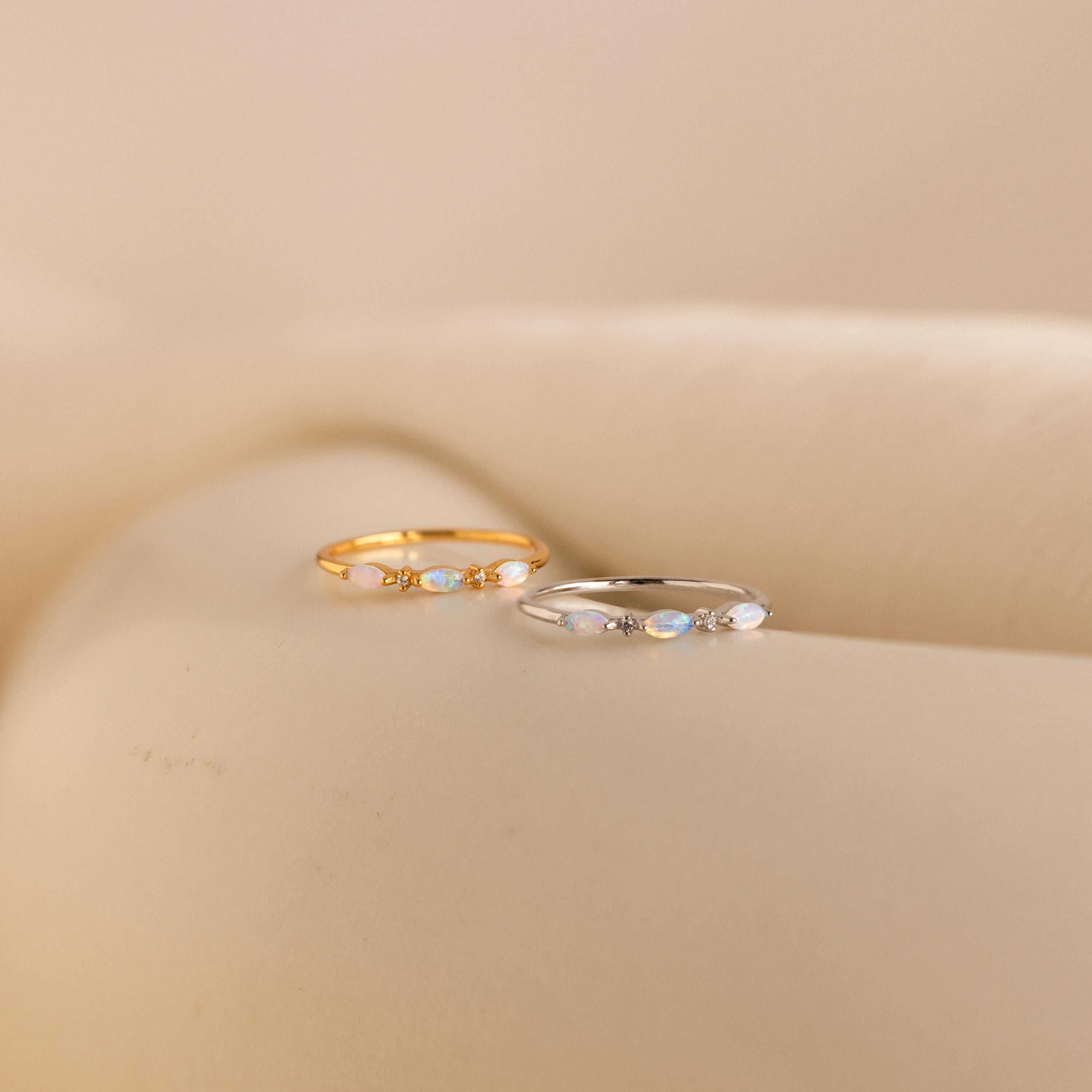 Side-by-side display of the Alessia Trio Opal Ring in gold and silver variations, each showcasing three marquise-cut opals with delicate diamond accents on slim bands, placed on a soft cream surface.