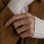 A hand wearing the Mini Toi et Moi Birthstone Ring, styled with a white sweater and a brown pinstripe coat.