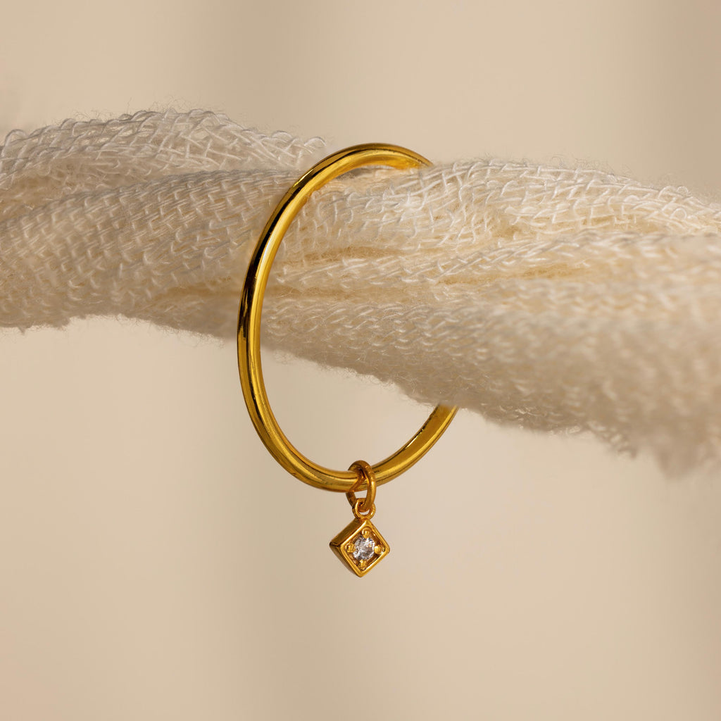 Gold hoop earring with a small diamond-shaped charm, hanging on a textured cream rope—perfect for pairing with your favorite Dainty Birthstone Drop Ring or other personalized jewelry.
