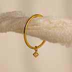 Gold hoop earring with a small diamond-shaped charm, hanging on a textured cream rope—perfect for pairing with your favorite Dainty Birthstone Drop Ring or other personalized jewelry.