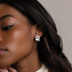 A woman with long dark hair wears Bold Square Wave Studs—shiny, chunky silver earrings—against a neutral background.