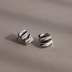 Bold Square Wave Studs in silver feature a wavy, textured surface for a unique touch. Displayed on a neutral background, these minimalist earrings add modern elegance to any luxury jewelry collection.