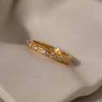 The Diamond Eternity Ring, a gold stackable band featuring a row of small round diamonds, is displayed on a soft beige surface.