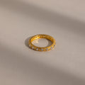 A Diamond Eternity Ring featuring small diamonds around the gold band, displayed on a softly lit neutral surface.