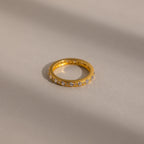 A Diamond Eternity Ring featuring small diamonds around the gold band, displayed on a softly lit neutral surface.