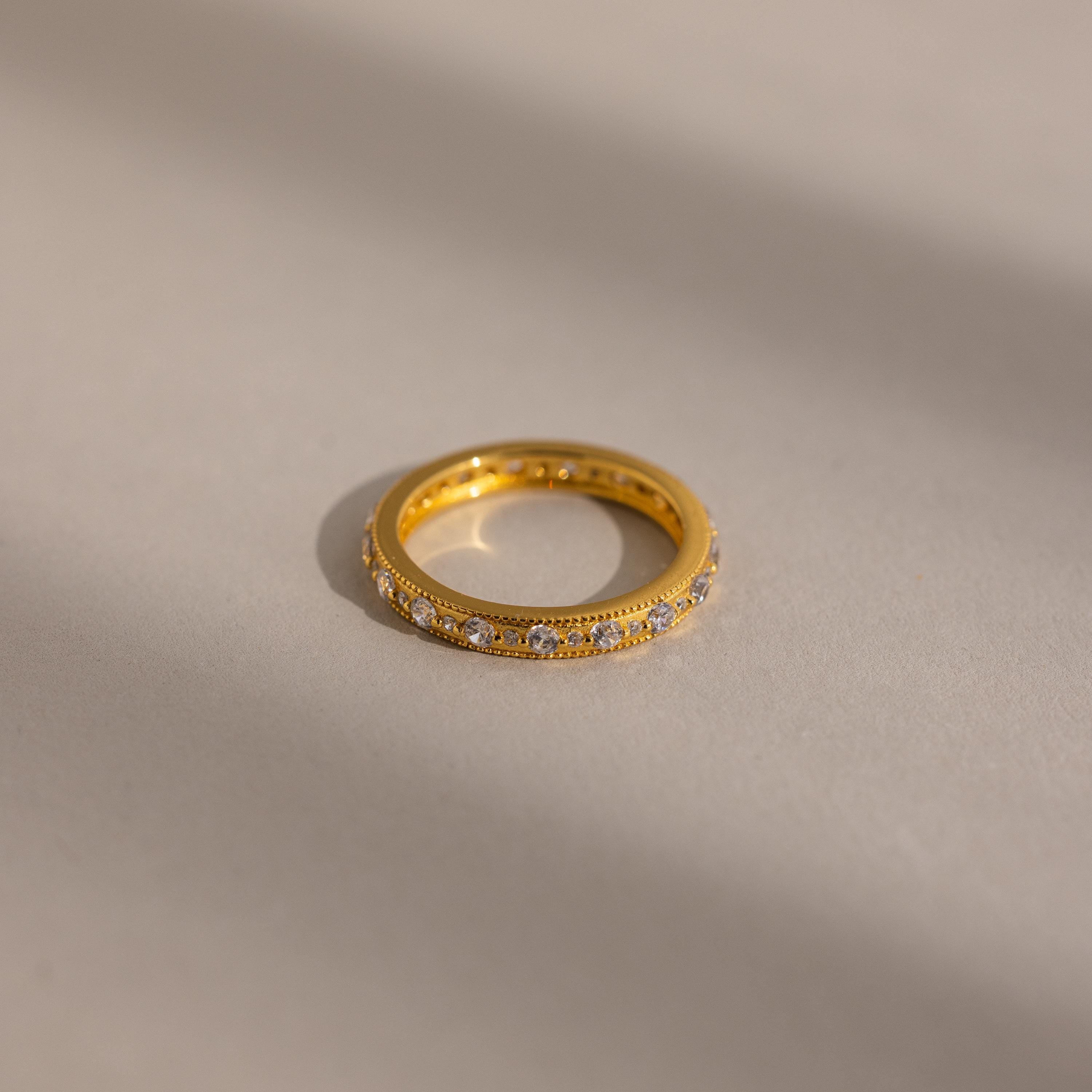 A Diamond Eternity Ring featuring small diamonds around the gold band, displayed on a softly lit neutral surface.