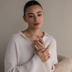 A woman wearing a cream ribbed sweater displays the Diamond Eternity Ring along with other gold stackable rings on her fingers, set against a neutral background.