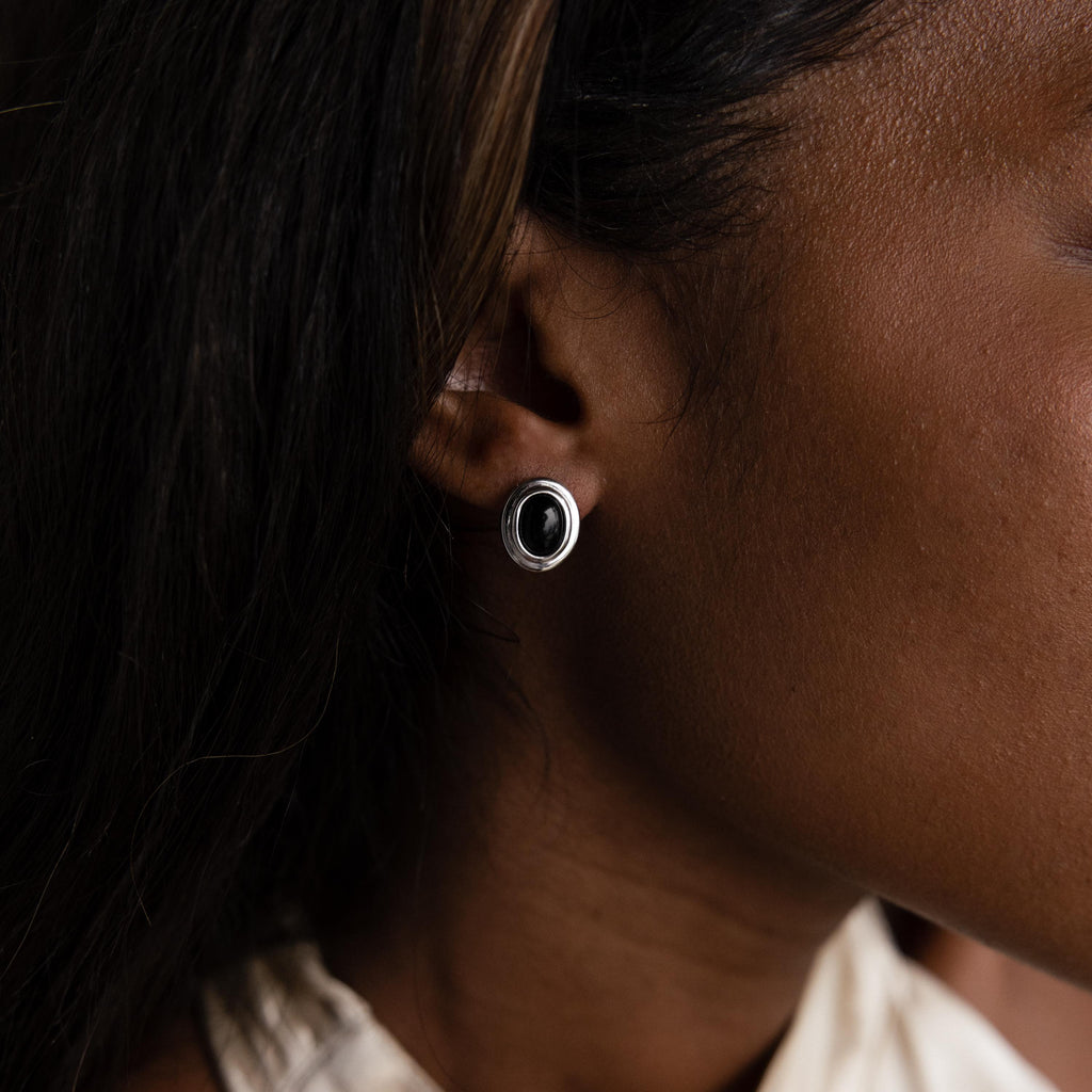 Close-up of a person wearing Vintage Oval Black Studs—retro silver statement earrings featuring a bold black center.