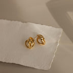 The Bold Multi Knot Studs feature an abstract, layered knot design and are displayed on textured white paper under soft lighting, highlighting their modern elegance.