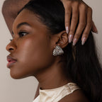 A woman with long hair wears Bold Triangle Knot Studs—shiny, sculpted silver earrings that catch the light as she touches her head, making a true statement accessory.