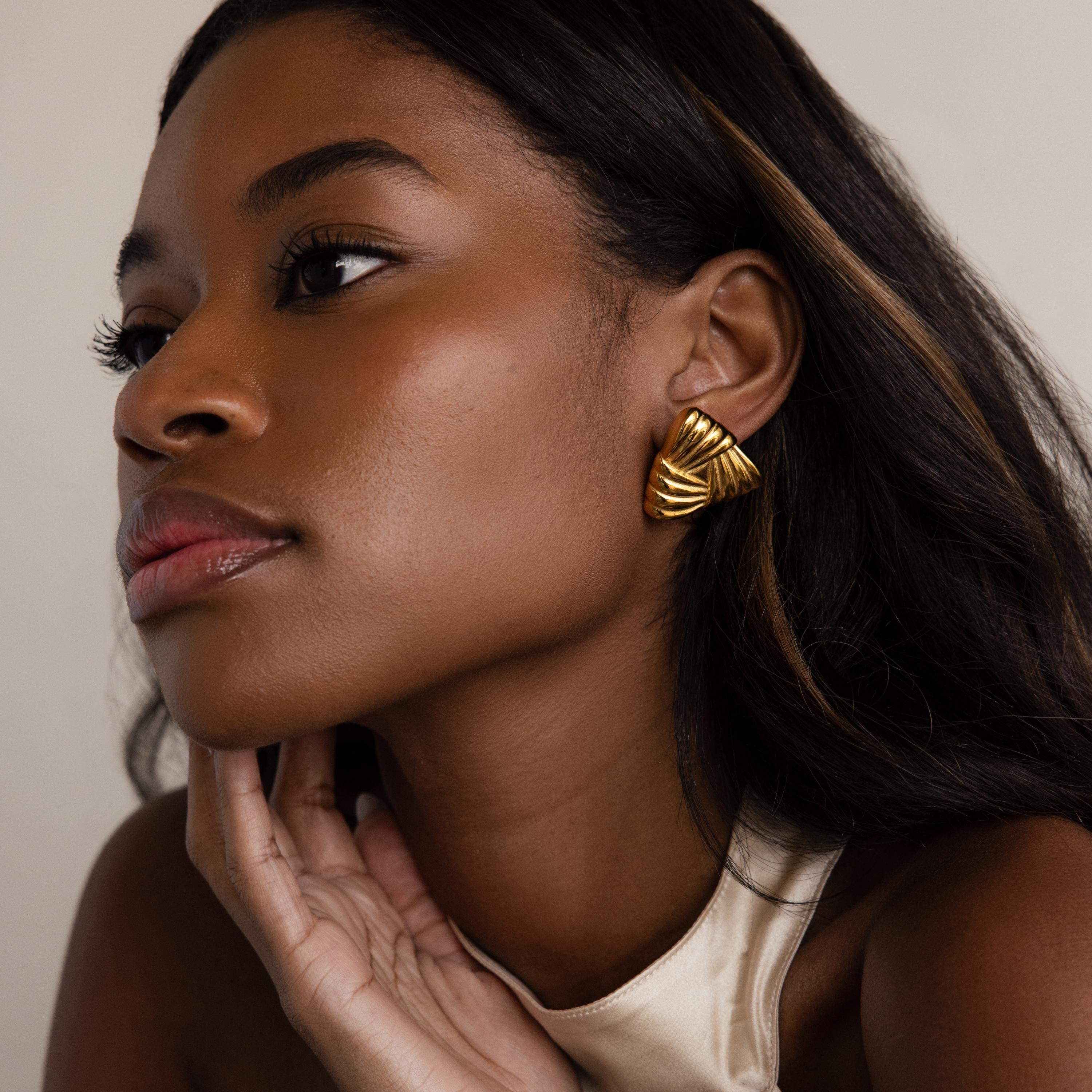 Woman with long hair wears Bold Triangle Knot Studs and a cream-colored top, looking thoughtful—these striking statement earrings are the perfect accessory for any occasion.