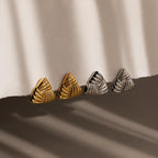 Two pairs of Bold Triangle Knot Studs—one gold and one silver—feature chunky, textured triangular designs and rest on a white fabric surface, creating a striking statement accessory for any look.